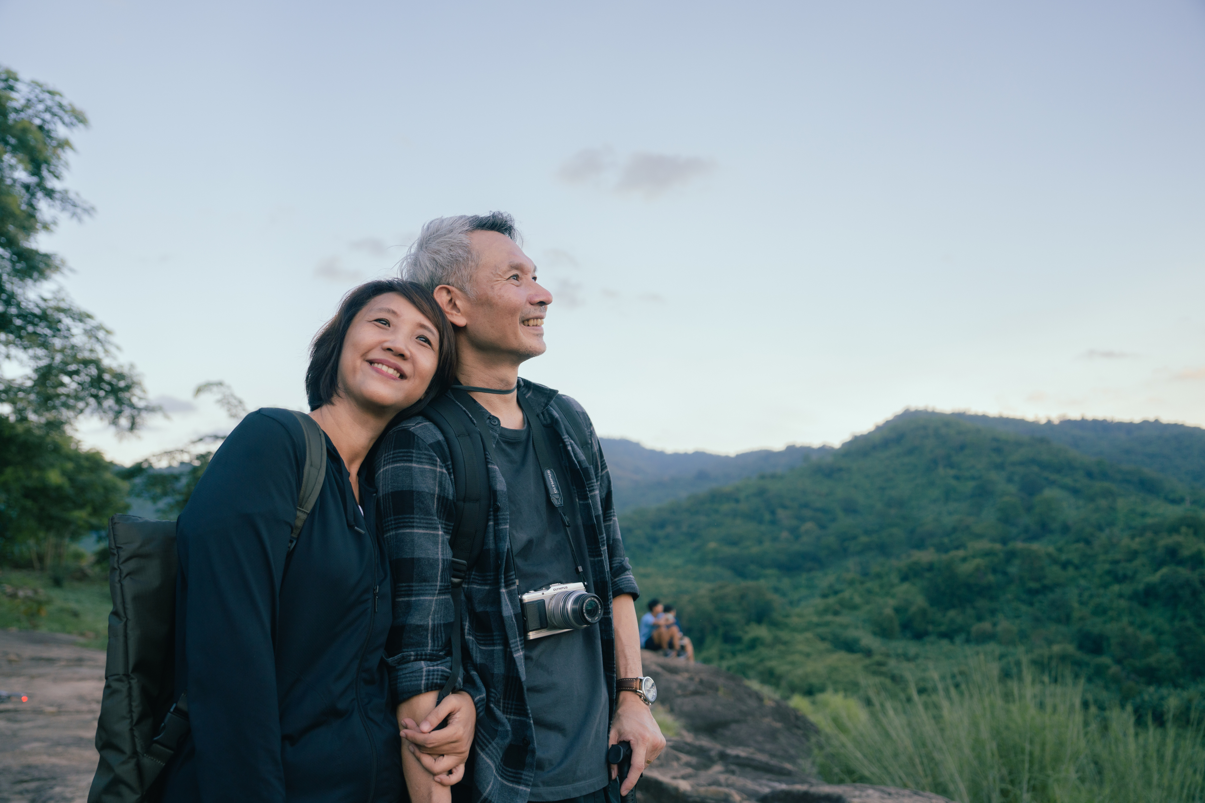 A couple stands together on a mountain top, enjoying the breathtaking view and embracing the moment whilst hiking.